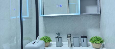 Un baño moderno con cabina de ducha de vidrio, lavamanos blanco, espejo y dos plantas en macetas.
