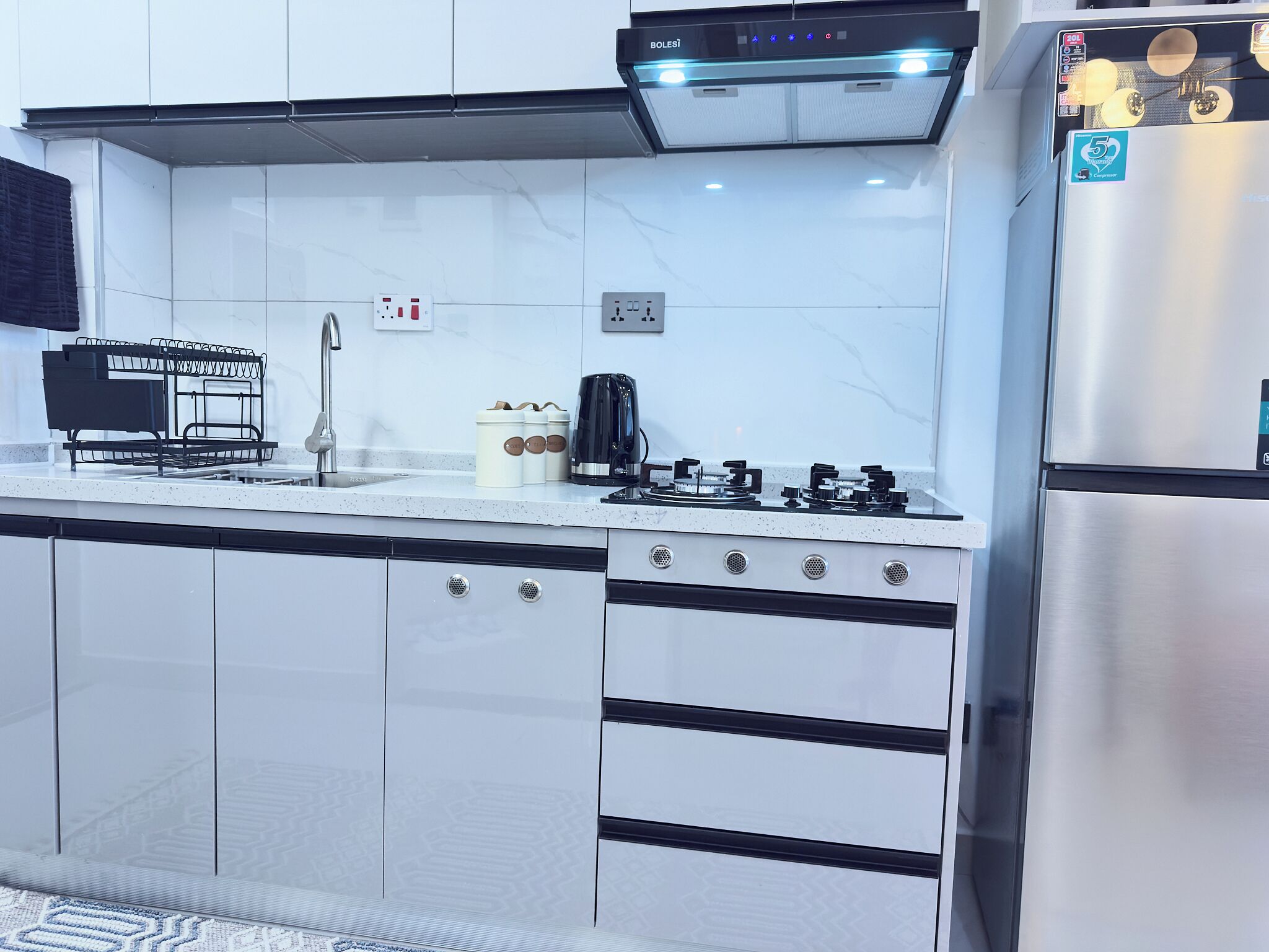 A modern kitchen with white cabinets, a stainless steel refrigerator, a gas stove, and a built-in oven.