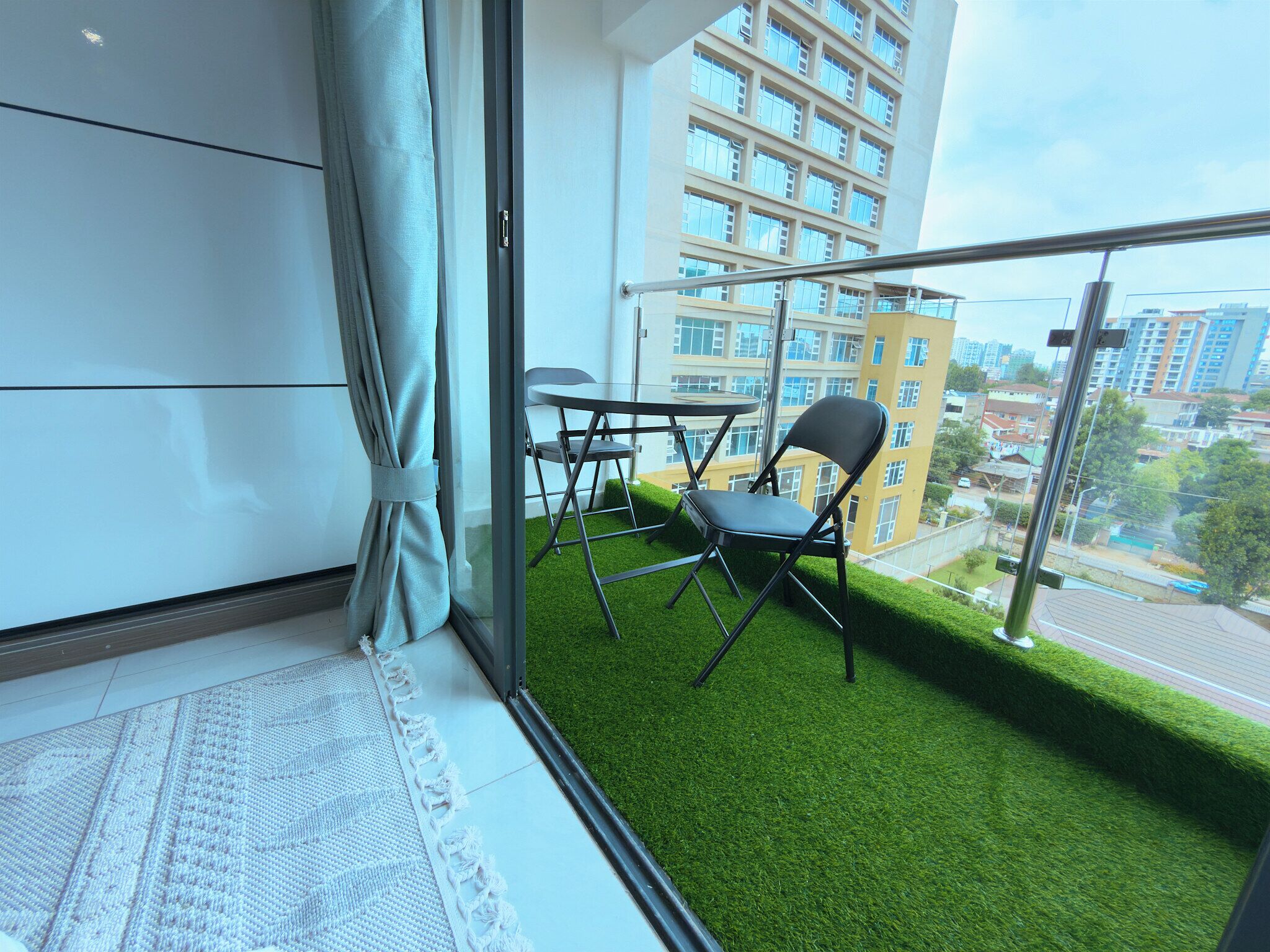 A balcony with artificial grass, a table, chairs, and a view of a cityscape.