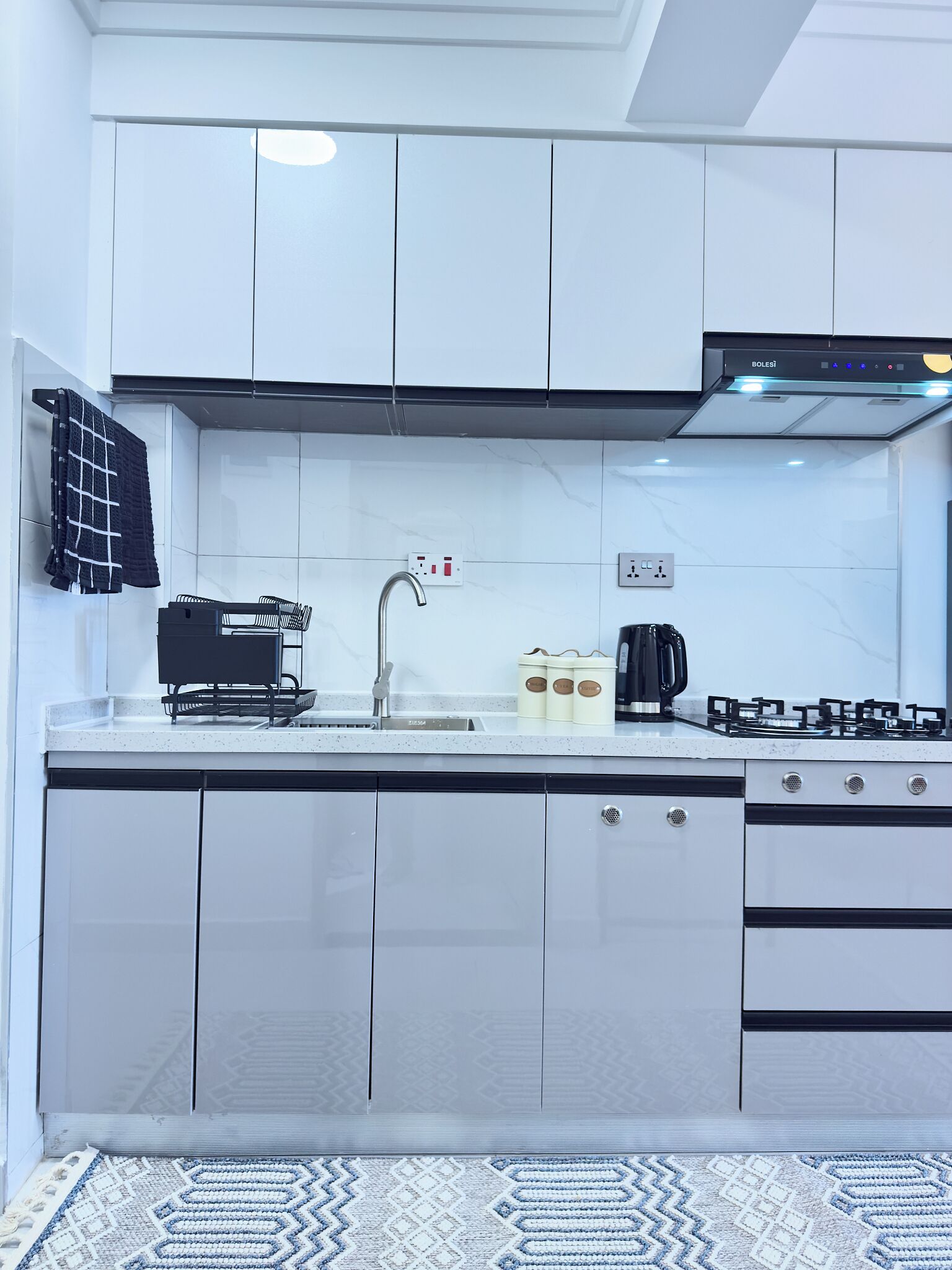 A modern kitchen with white cabinets, a stainless steel sink, a gas stove, and a coffee maker.