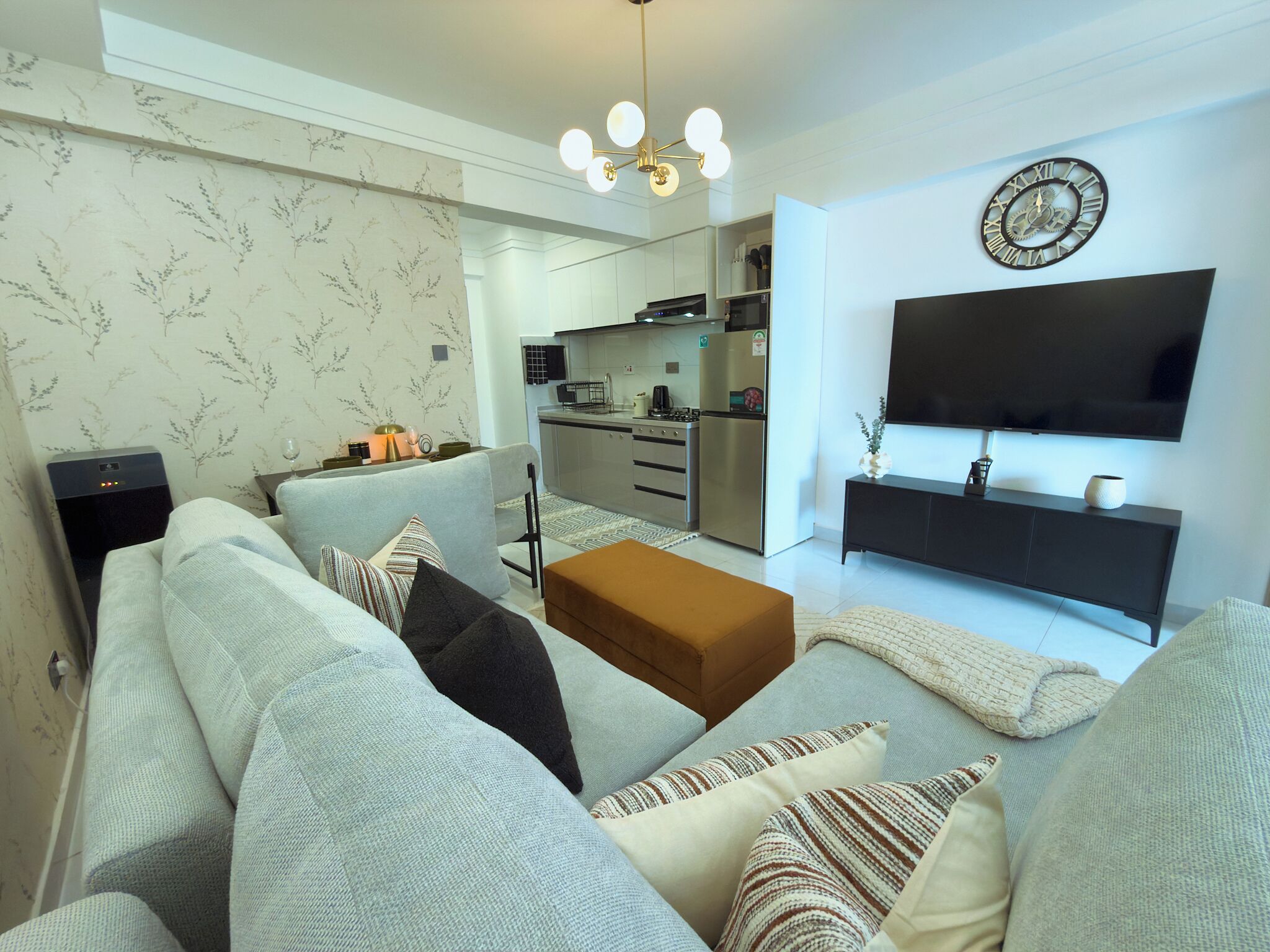 Una sala de estar moderna con un sofá, una mesa de centro, un televisor y una cocina al fondo.