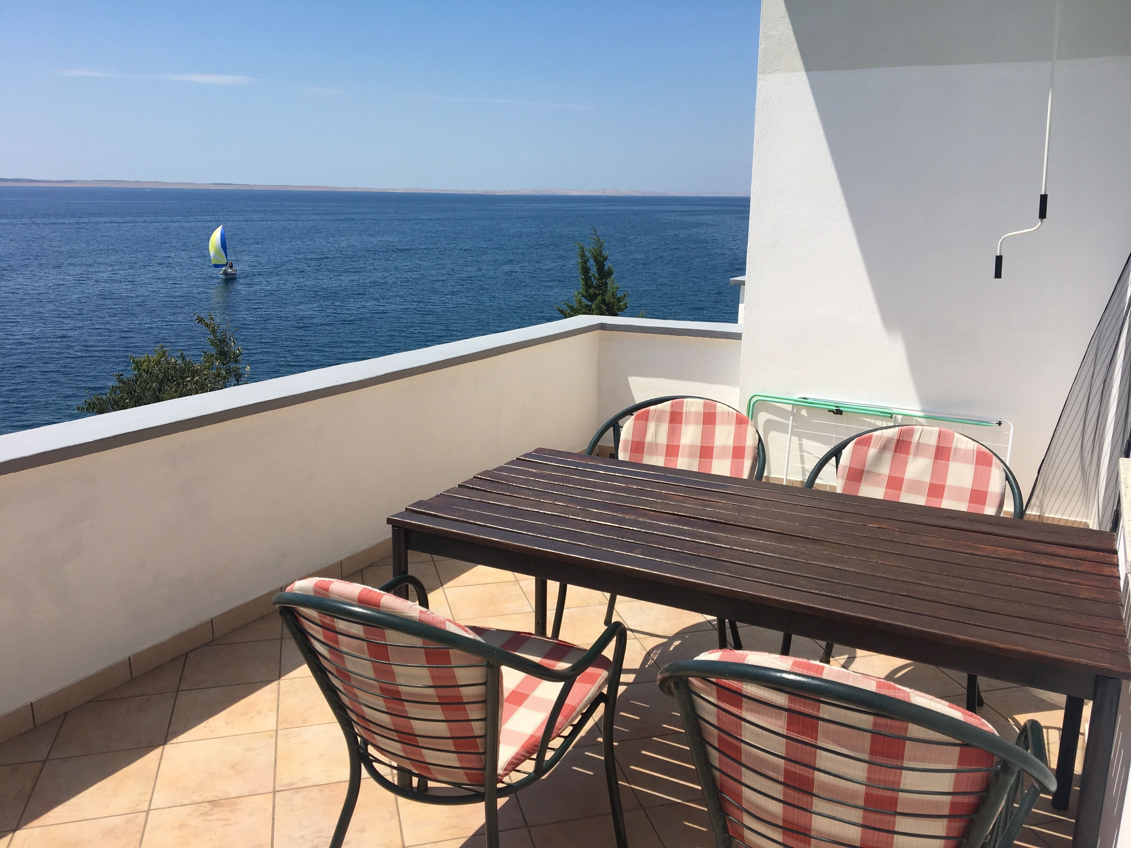 A balcony with a table and chairs, overlooking the sea with a sailboat in the distance.