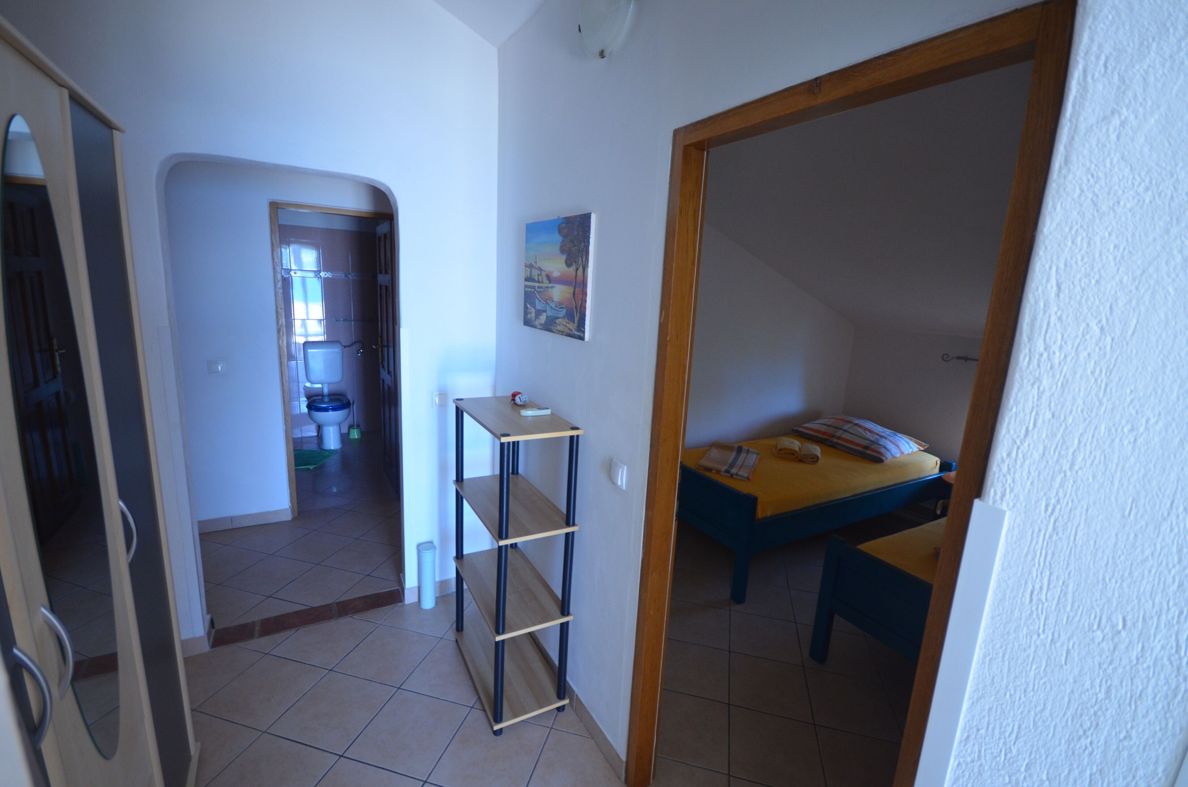 Ein Zimmer mit einem Bett, einem kleinen Tisch, einem Regal und einem Gemälde an der Wand.