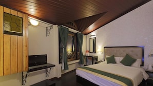 Ein Hotelzimmer mit Bett, Schreibtisch, einem Fenster mit Vorhängen, einem Spiegel und einer Holzbalkendecke.