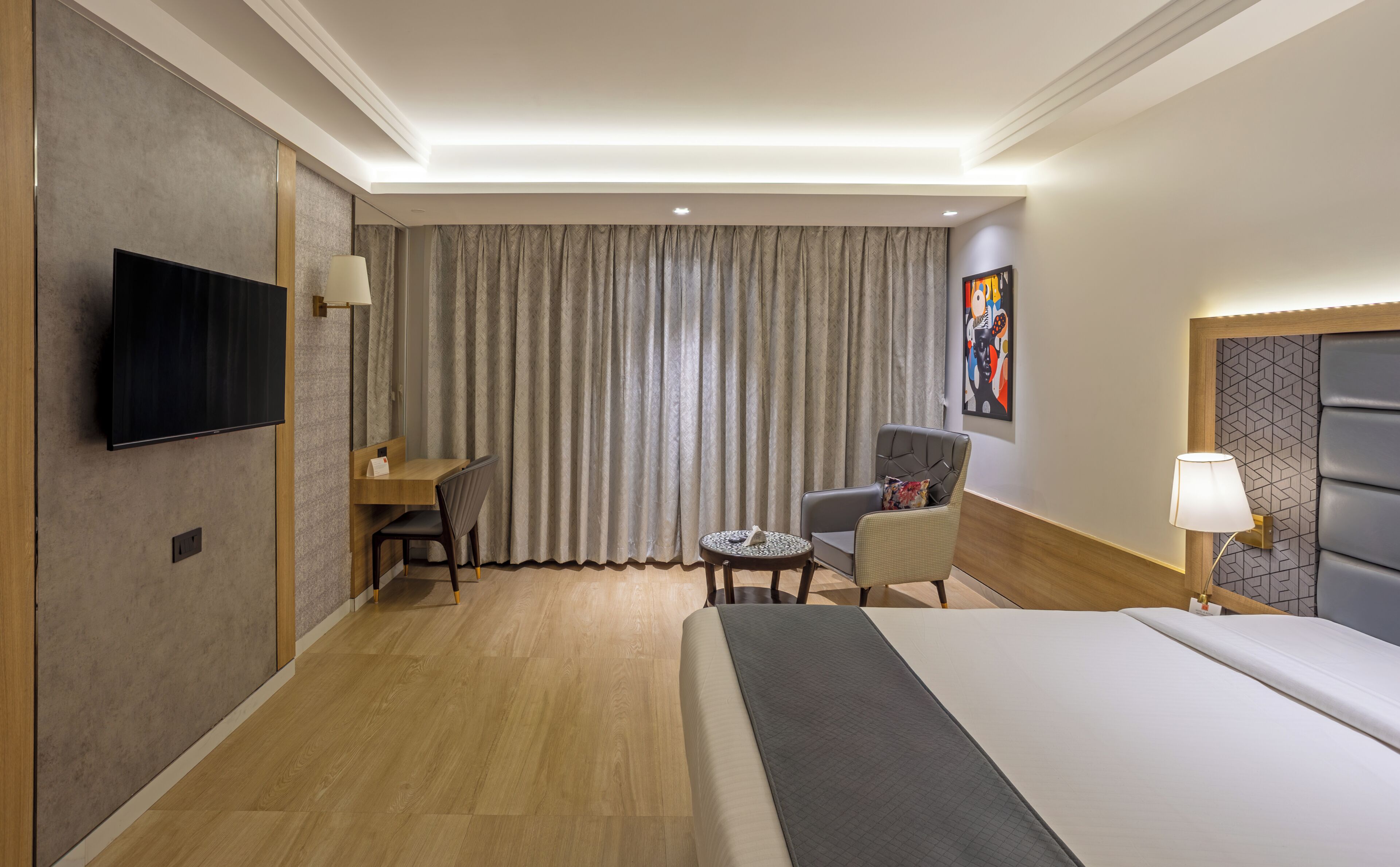 A hotel room with a bed, a desk, a chair, a television, and a painting on the wall.