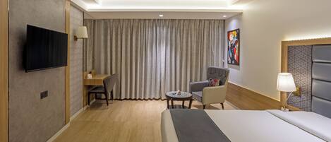 A hotel room with a bed, a desk, a chair, a television, and a painting on the wall.