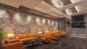 A lobby with sofas, a coffee table, a large wall with a marble-like texture, and a chandelier. - Hill Berry - A SoVo Hotel (Mawal)