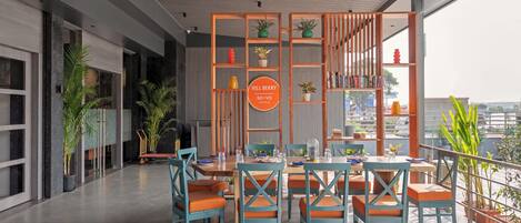 A modern hotel lobby with a dining area, potted plants, and a sign for Hill Berry So'Vo Hotels.