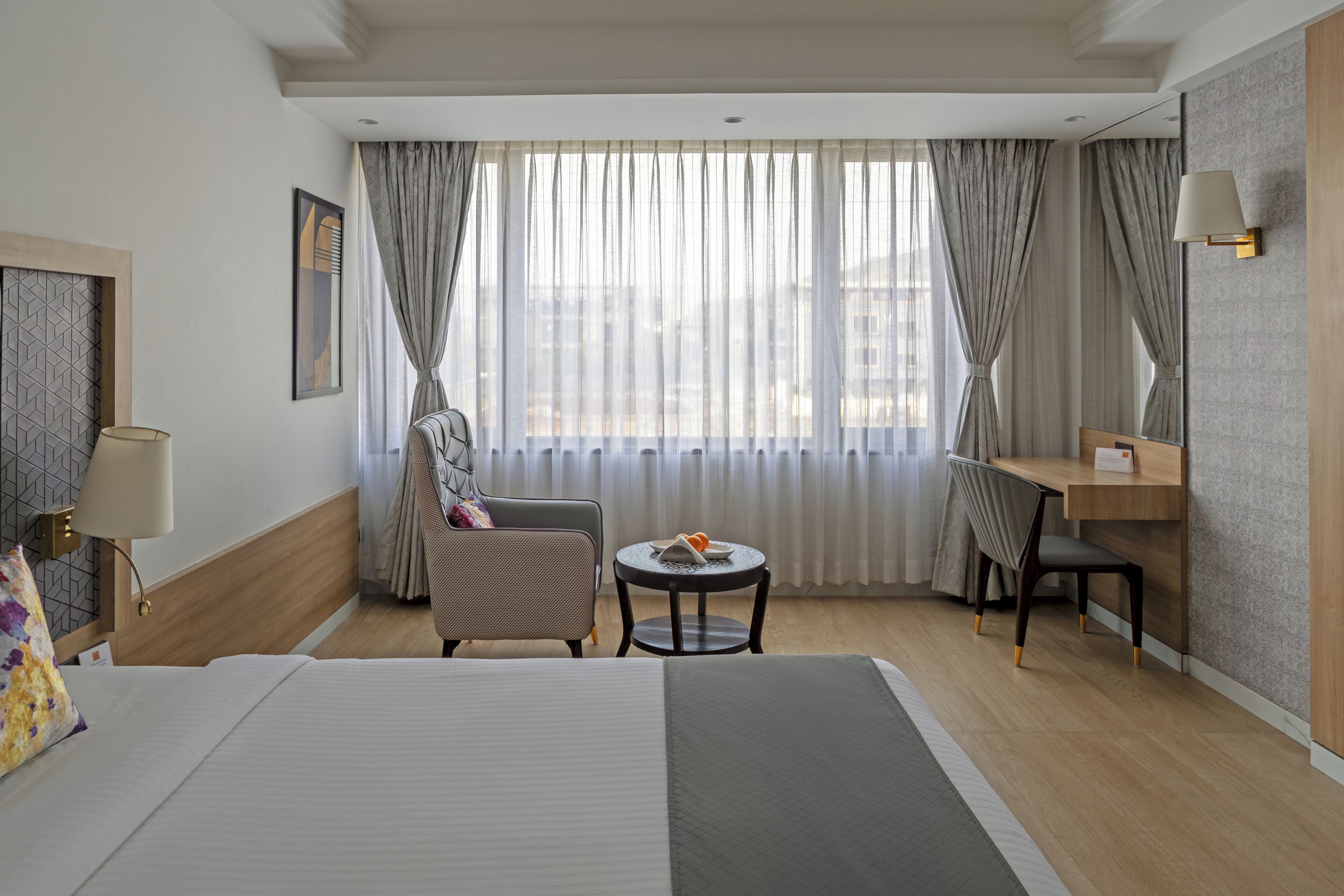A hotel room with a bed, a desk, a chair, a small table, and a window with curtains.