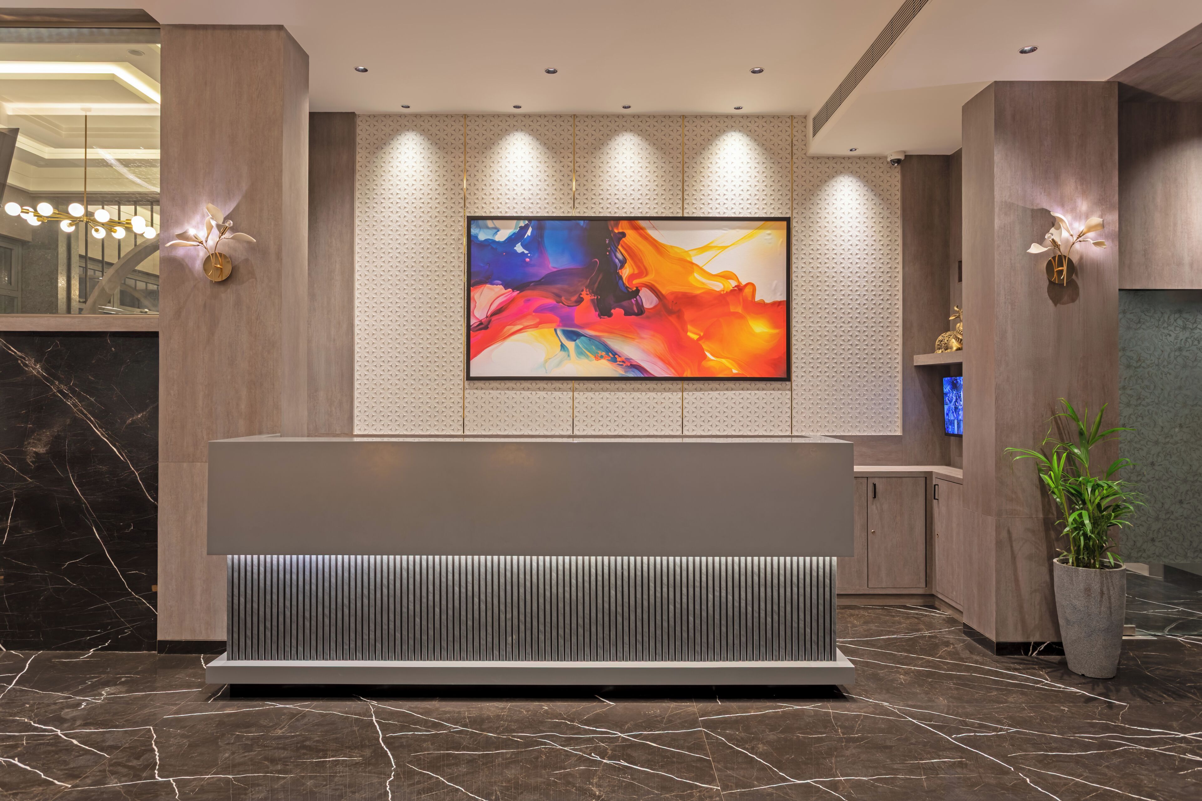 A reception desk with a modern design, a large abstract painting, and a potted plant.