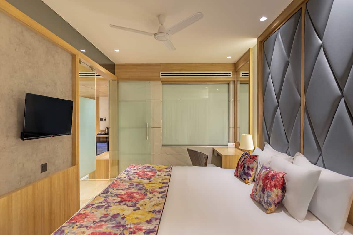 Una habitación de hotel moderna con una cama, televisión, ventilador de techo y un ventanal grande.