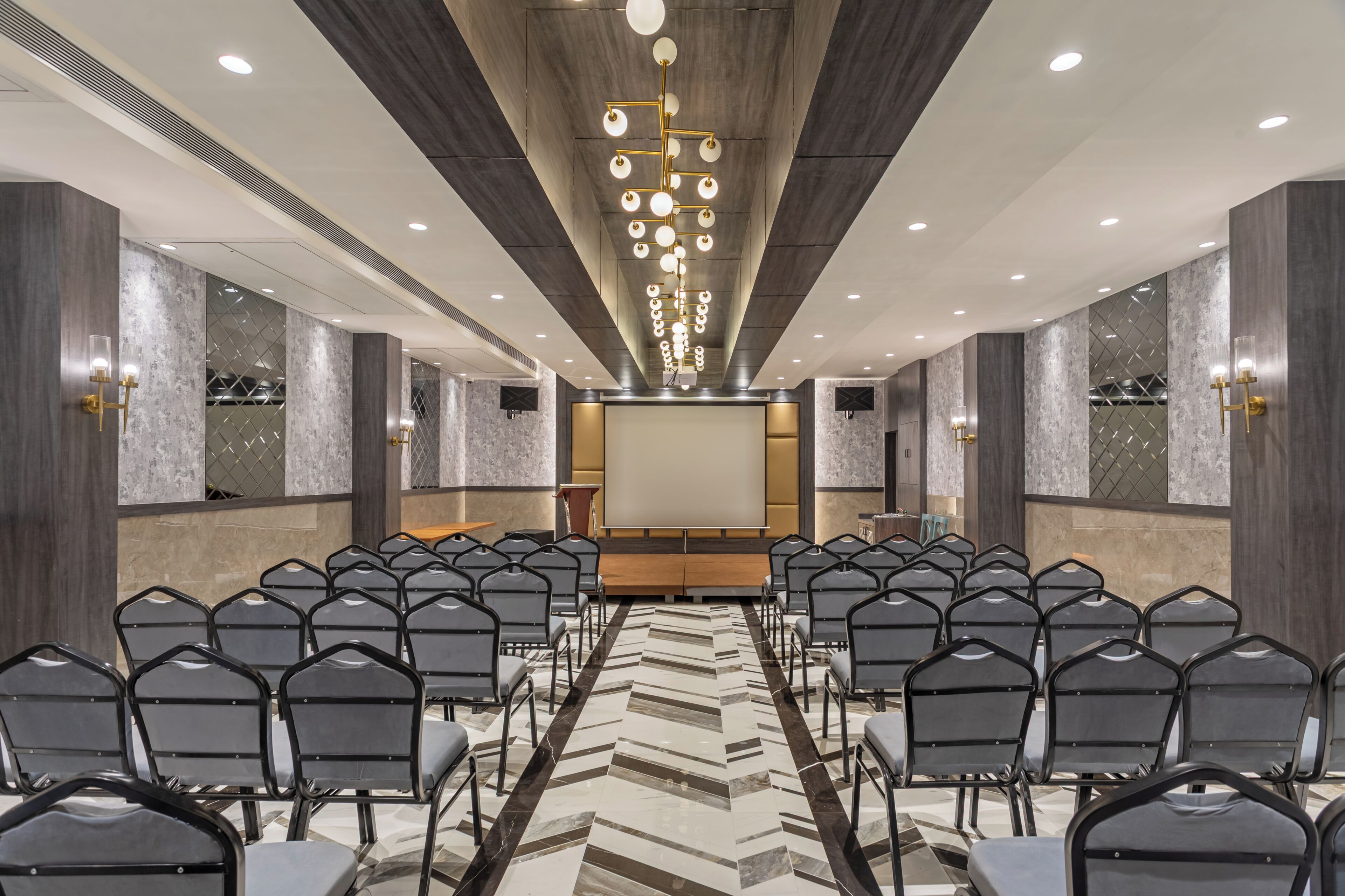 A conference room with rows of chairs, a projector screen, and a modern chandelier.