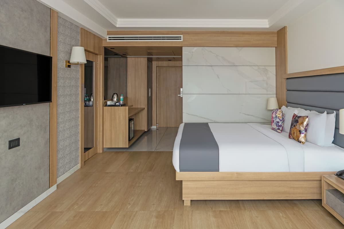 Habitación de hotel moderna con una cama grande, un televisor de pantalla plana, un armario de madera y un escritorio integrado con una lámpara.