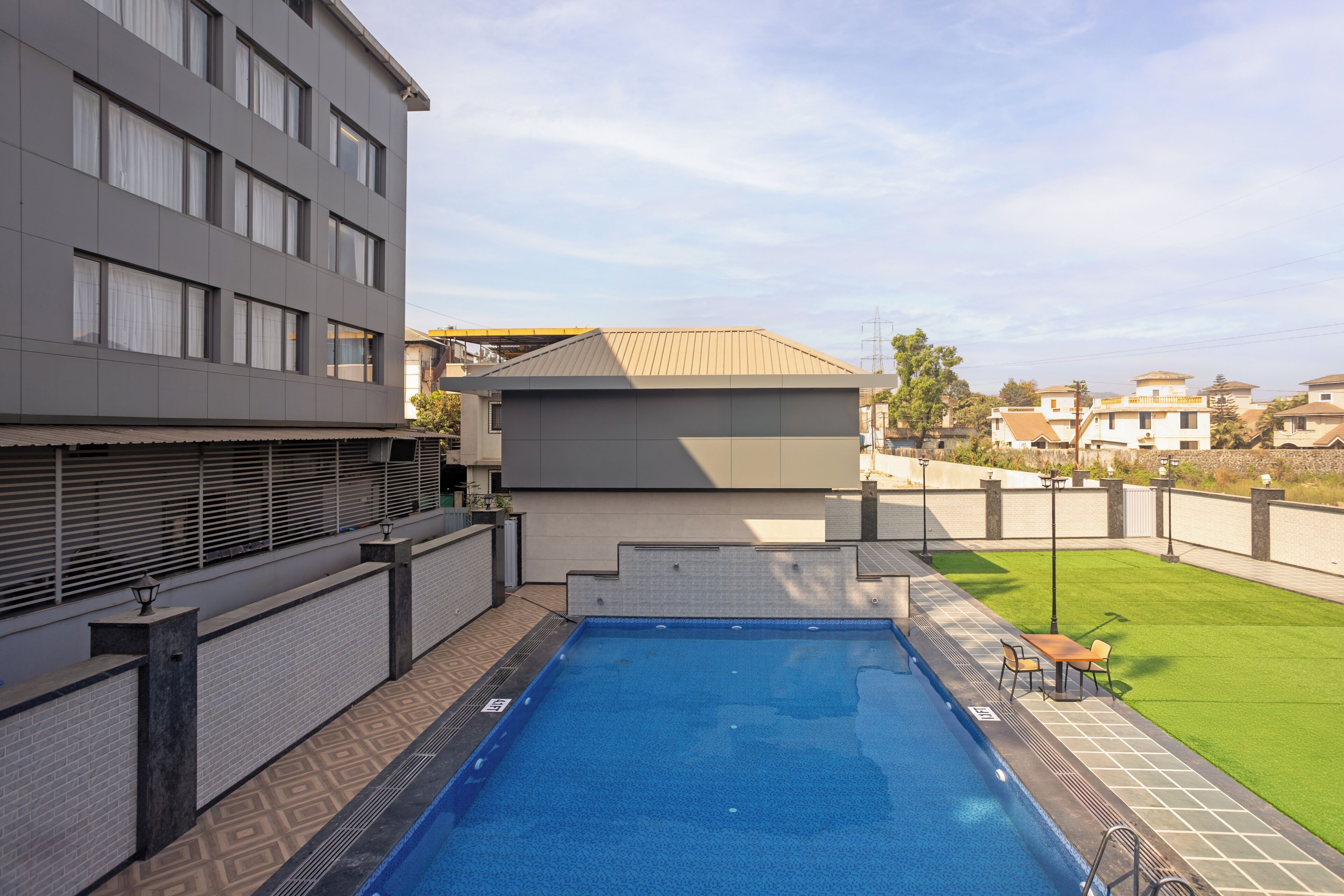 Una piscina con borde de baldosas, una pequeña mesa y sillas, y vistas de edificios circundantes.