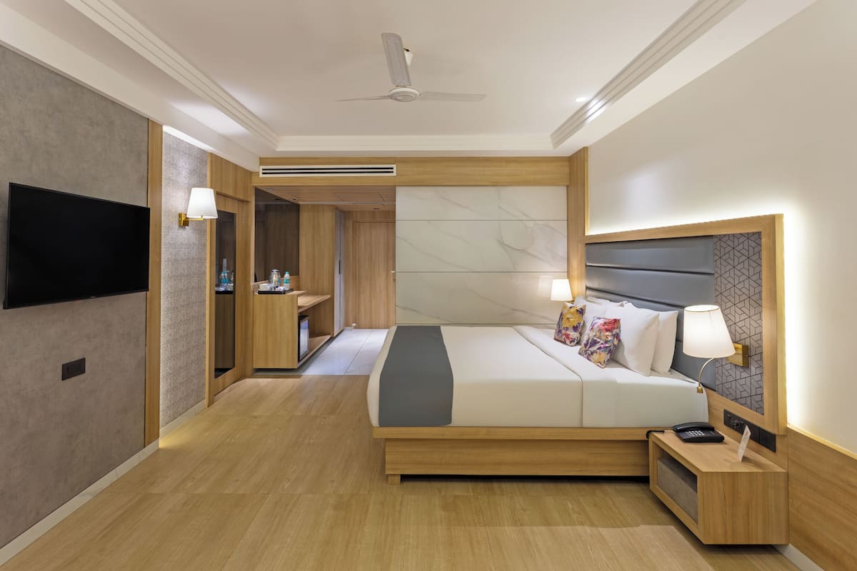 Una habitación de hotel moderna con una cama grande, un televisor de pantalla plana, una mesita de noche con lámpara y un armario empotrado.