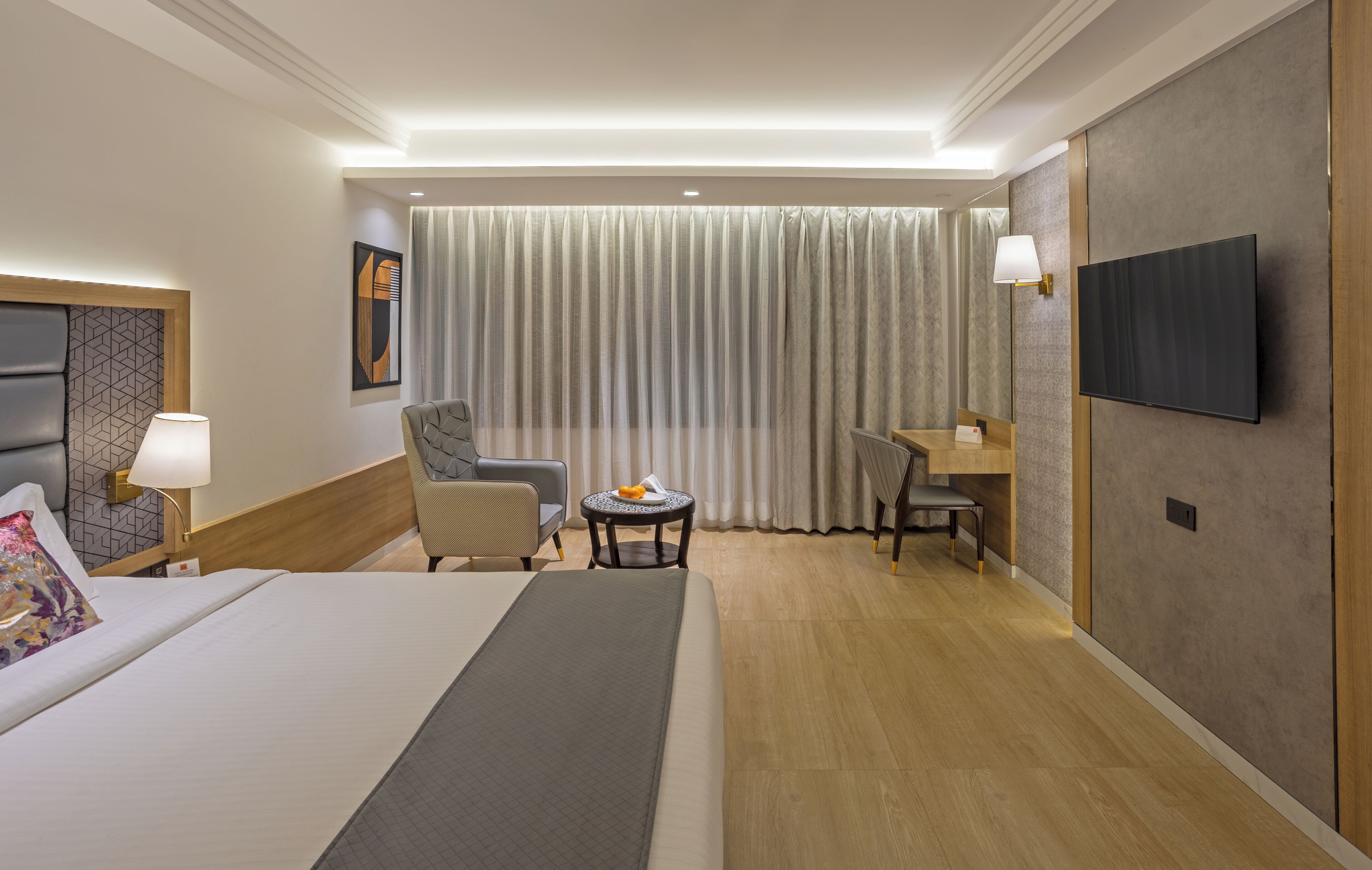 Habitación de hotel con cama, escritorio, silla, televisor y ventana con cortinas.