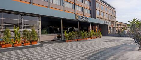 A hotel with a modern facade, a checkered tile floor, and potted plants along the entrance.