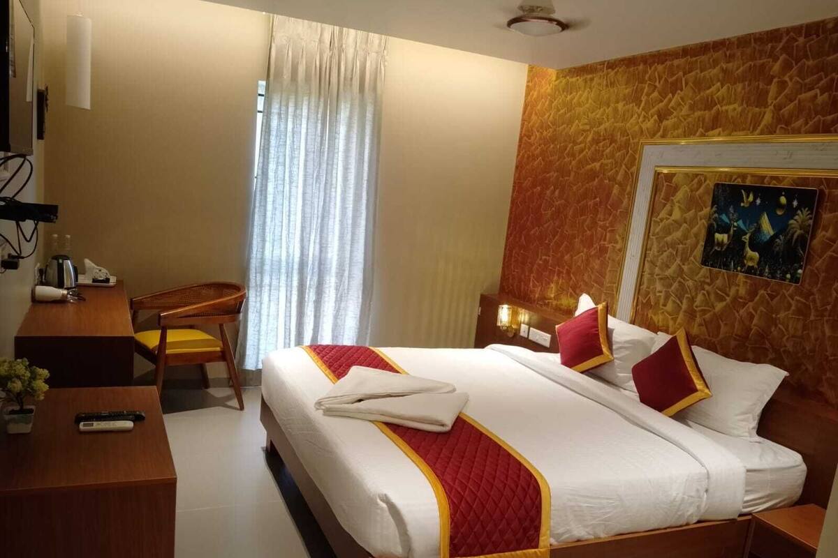 A hotel room with a bed, a desk, a chair, a nightstand, and a painting on the wall.
