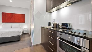 Een moderne hotelkamer met een bed, kitchenette en een groot abstract schilderij aan de muur.