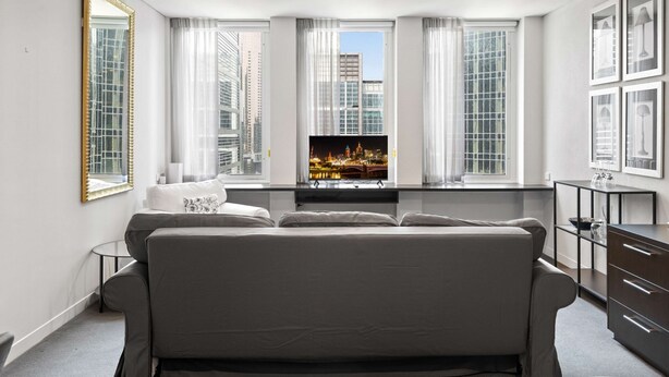 Een moderne hotelkamer met een groot bed, een aan de muur bevestigde televisie en uitzicht op de stad door grote ramen.
