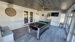 Een kamer met een tafeltennistafel, een plafondventilator en een aan de muur bevestigde televisie.