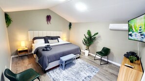 A modern bedroom with a bed, bedside tables, a TV, a chair, a plant, and a small bench. - NONA Luxe 5BR 4BH  w/ Guesthouse / Theatre / GameRoom / Gym / Loft (Unknown)