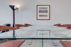 Une salle de conférence avec une table en verre, des chaises marron, un tableau encadré au mur et un lampadaire.