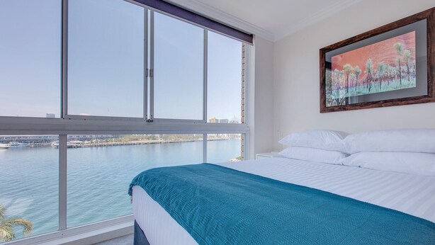 A bedroom with a large window, a bed with white linens, and a painting on the wall. - Wake up to Sydney Harbour (Balmain East)
