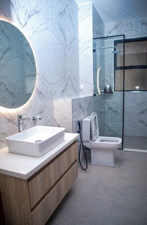 A modern bathroom with a marble vanity, a sink, a toilet, and a glass shower enclosure.