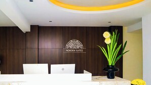 A reception desk with a marble top, a logo for 'NORDEN SUITES,' and two potted plants with yellow flowers. - Norden Suites (Mombasa)