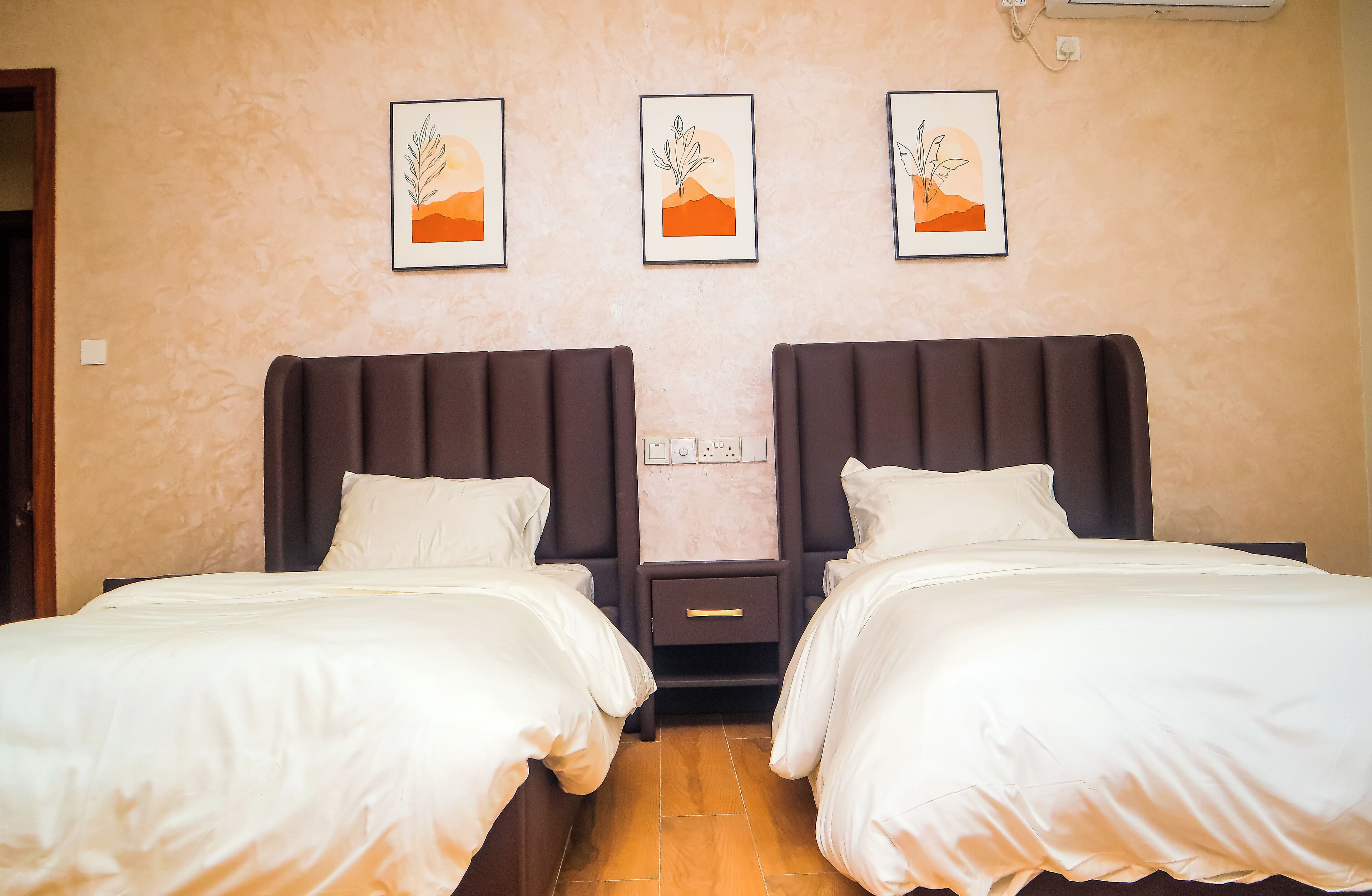 A double room with two beds, a nightstand, and three framed artworks on the wall.