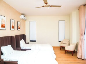 A hotel room with a bed, a chair, a ceiling fan, and artwork on the wall.