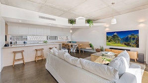 Une cuisine moderne avec un îlot central, un coin repas avec une table et des chaises, un canapé et un grand tableau représentant un paysage accroché au mur.