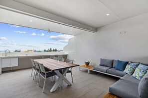 A modern kitchen with a dining area, a sofa, and a view of the sky. - Luxury 5-floor Unit with Ocean Views near Beach (Caloundra)