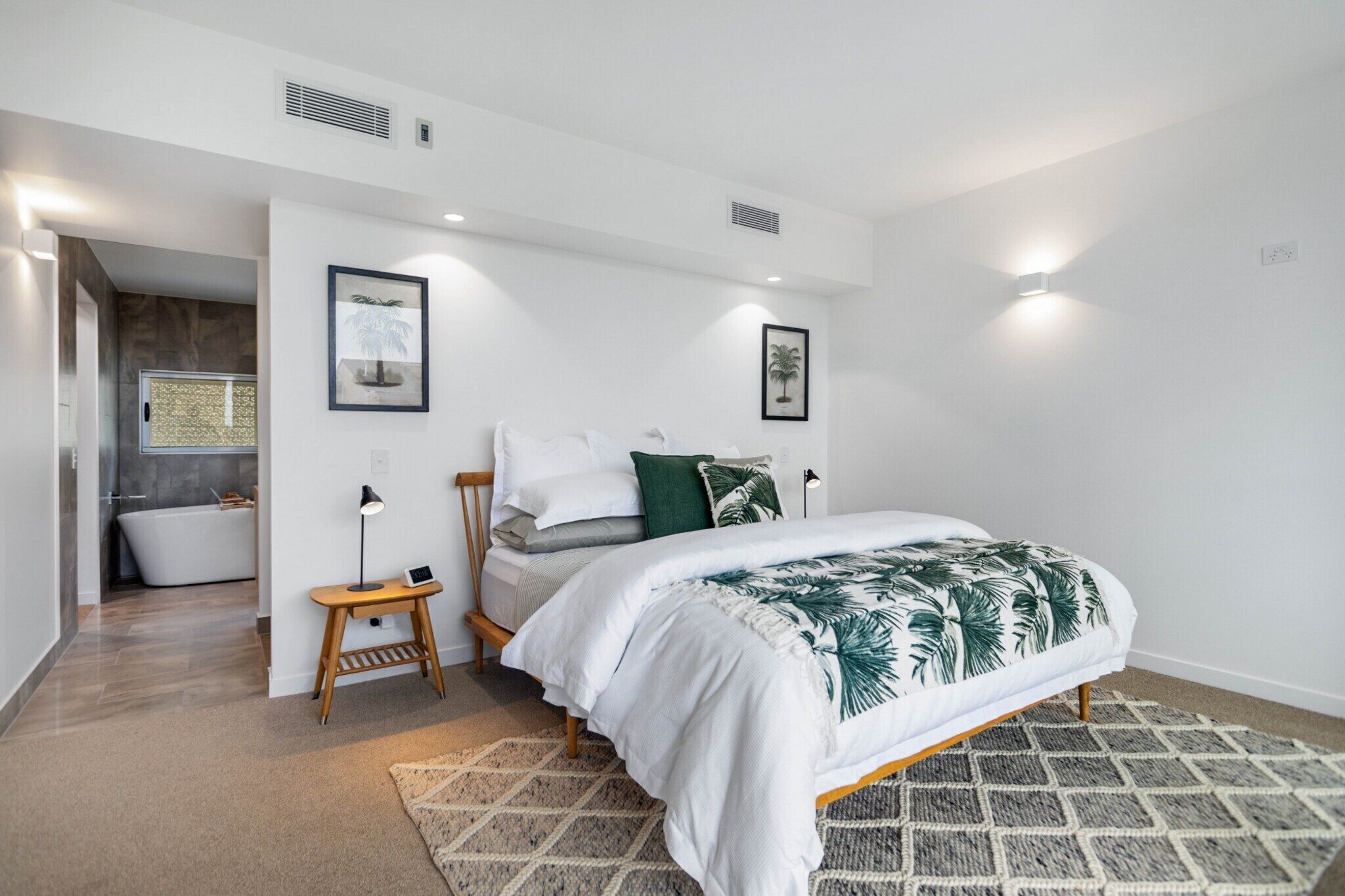 A modern bedroom with a bed, bedside tables, and a bathroom in the background.