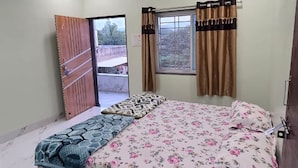 A bedroom with a bed, a ceiling fan, a window with curtains, and a door.