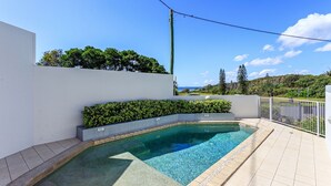 Une piscine dotée d’une terrasse carrelée, entourée d’un mur blanc et d’une haie.