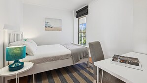 Une petite pièce propre, avec un lit, un bureau, une chaise, une lampe, une fenêtre et un tableau accroché au mur.