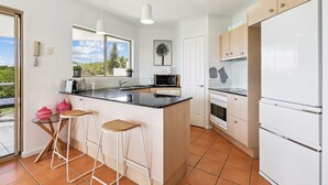 Une cuisine moderne dotée d’un grand îlot central, de meubles blancs et offrant une vue sur l’extérieur.