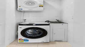 Een compacte wasruimte met een Samsung wasmachine en droger, een klein wasbakje en een wand betegeld met witte tegels.