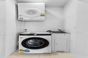 A compact laundry room with a Samsung washer and dryer, a small sink, and a white tiled wall. - Spacious and Superb 3-Bed Apartment (Bulimba)