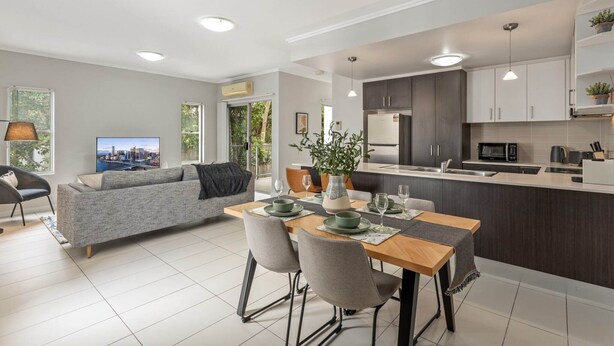 Una cocina moderna con armarios oscuros, una mesa de comedor para cuatro personas y un amplio ventanal con vistas a la ciudad.