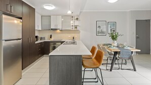 Una cocina moderna con una isla central, armarios de madera oscura, electrodomésticos de acero inoxidable y un comedor con mesa y sillas.