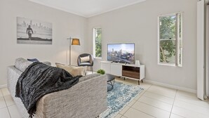Una sala de estar con un sofá, televisión, lámpara y una pintura de un paisaje urbano.