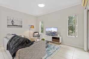A living room with a sofa, a television, a lamp, and a cityscape painting. - Central Cosy 2-Bed with Pool and near QUT & CBD (Kelvin Grove)