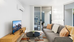 Una sala de estar moderna con una televisión, un sofá, una mesa de centro y un ventanal corredizo que da a un balcón.