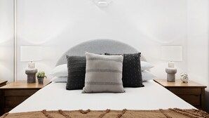 Un dormitorio con una cama, dos mesitas de noche, una lámpara, un reloj y una planta pequeña.