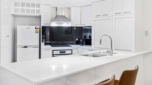 Una cocina moderna con armarios blancos, una campana de acero inoxidable, horno empotrado y una isla grande con un lavamanos.