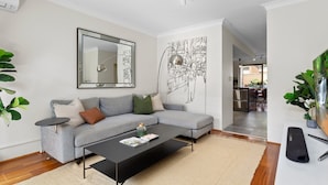 Ein modernes Wohnzimmer mit grauem Sofa, einem schwarzen Couchtisch, einem großen Spiegel und einem Wandbild.