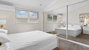 Ein modernes Schlafzimmer mit einem großen Bett, einem Spiegel und einem Fenster mit Jalousien.